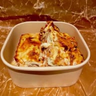 En portion lasagne i en engångsmatlåda.