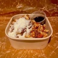 Takeoutlåda med pastaskruvar i köttig sås, toppad med riven ost och en liten såsbehållare.