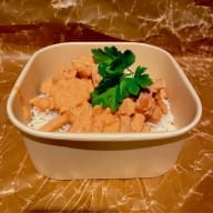 Takeawaylåda med ris täckt av krämig gryta och en persiljekvist.