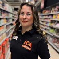 En ICA-medarbetare i butikskläder står i en butiksgång.