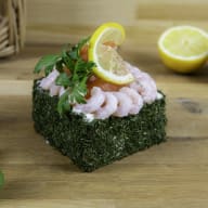 En rätt med räkor och citronskiva serveras på ett fyrkantigt underlag på ett träbord.