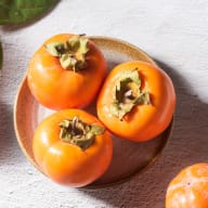 Tre sharonfrukter som ligger på ett fat. Orange i färgen.