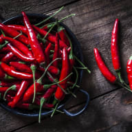 En skål med chilifrukter står på en träyta bredvid några lösa chilifrukter.