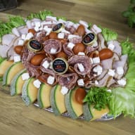 Ett fat med charkuterier, ost, grönsaker och frukt är upplagt på ett bord.