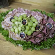 Ett fat med skivat kött, druvor och salladsblad är upplagt på ett bord.