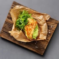 En smörgås med avokado och sallad ligger på ett träbord med brunt papper.
