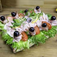En sallad med räkor, oliver och grönsaker ligger på ett träbord.