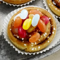 En tallrik med olika små bakverk och cupcakes står på ett bord tillsammans med skålar fyllda med godis och frukt.