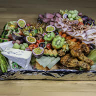En bricka med olika sorters mat inklusive frukt, grönsaker, ost, kött och charkuterier ligger på ett träbord.