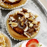 En tallrik med olika små bakverk och cupcakes står på ett bord tillsammans med skålar fyllda med godis och frukt.