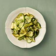 En tallrik med skivad och marinerad zucchini står på ett bord.