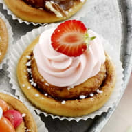 En tallrik med olika små bakverk och cupcakes står på ett bord tillsammans med skålar fyllda med godis och frukt.