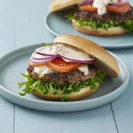 välfylld hamburgare på en blå tallrik stående på ett blått träbord med en likadan hamburgare i bakgrunden