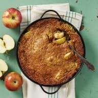 Knäckig äppelpaj i en gjutjärnsform. Pajen står på tygservett. Grön bakgrund.