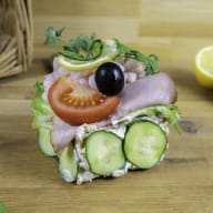 En smörgås med skinka, grönsaker och en oliv ligger på ett träbord bredvid citroner.