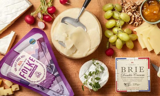 En träskärbräda med olika sorters ost, bland annat ICA Folke och ICA Brie. Där finns också vindruvor, rädisor och en marmelad.