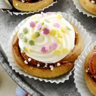 En tallrik med olika små bakverk och cupcakes står på ett bord tillsammans med skålar fyllda med godis och frukt.