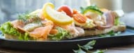 landgång med ljust bröd, lax, skinka dekorerad med grönsaker serverat på ett svart fat