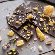 Bitar av mörk choklad med nötter och torkad frukt ligger utspridda på en yta.