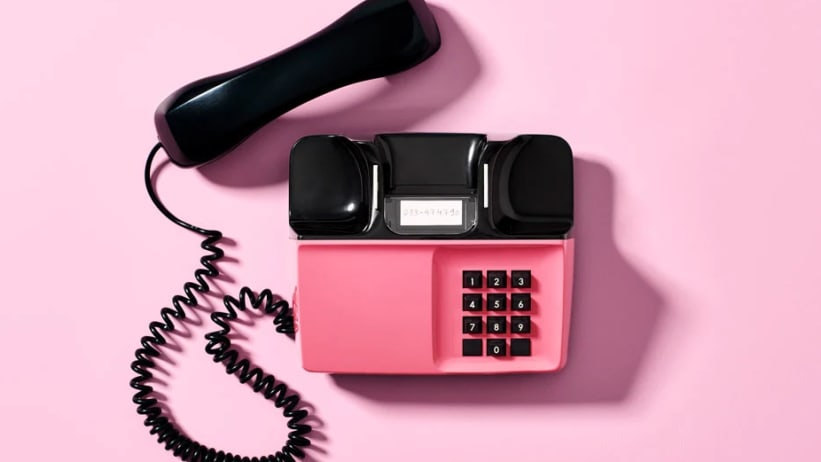 En rosa telefon med svart handtag på en rosa bakgrund.
