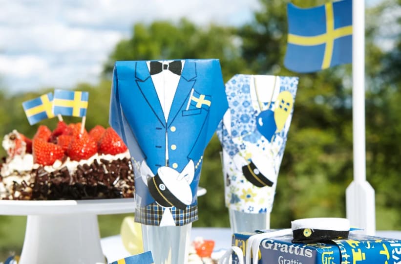 Festlig dukning utomhus för studentskiva, med svenska flaggor, jordgubbstårta, studentmössor och presenter.