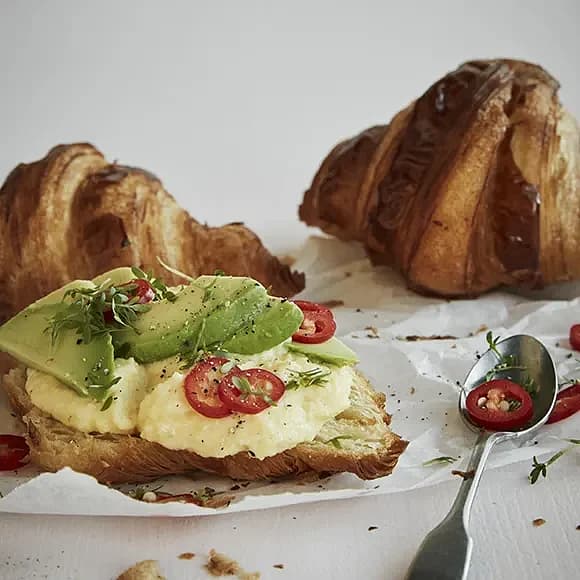 Croissant till frukost med krämig äggröra, avokado och chili