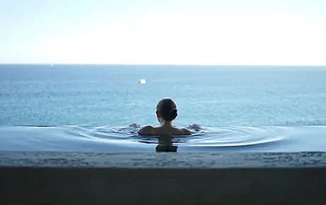 En kvinna ligger i en pool på en spaanläggning och blickar ut över vattnet.